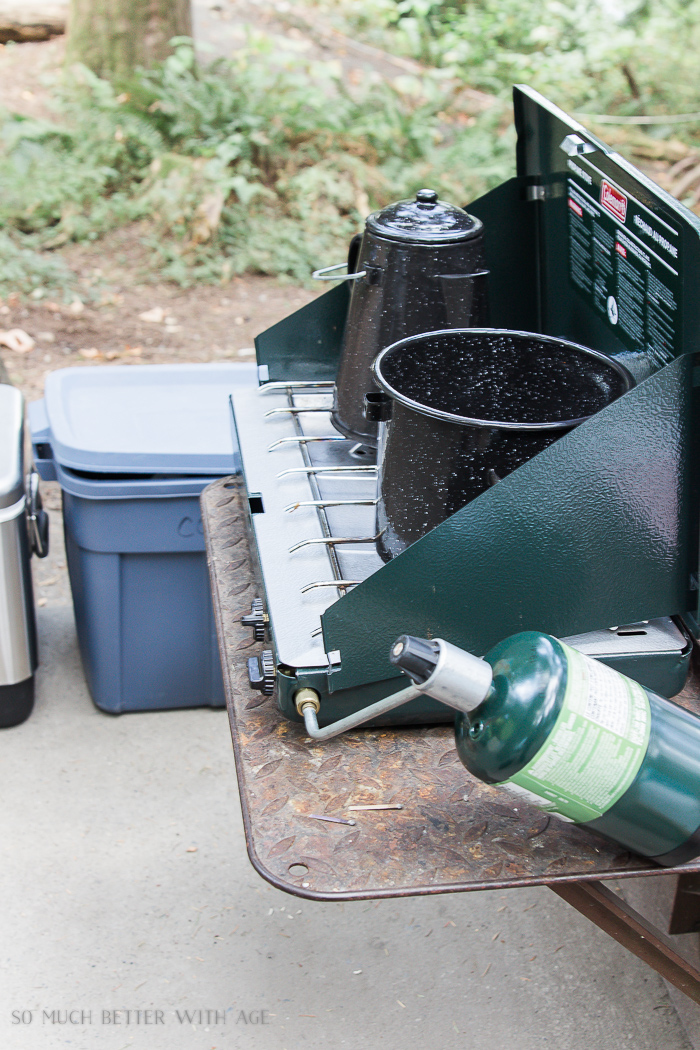 Camp stove with pot on it and bins in the background.