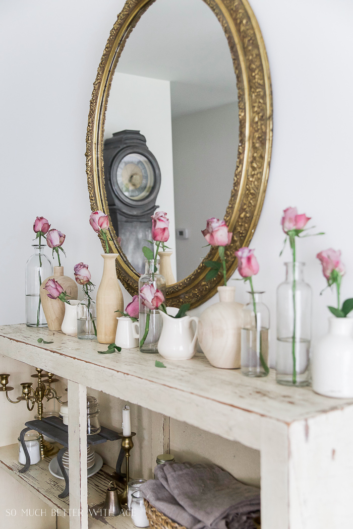 Pink roses in clear vases singular on the wooden mantel.