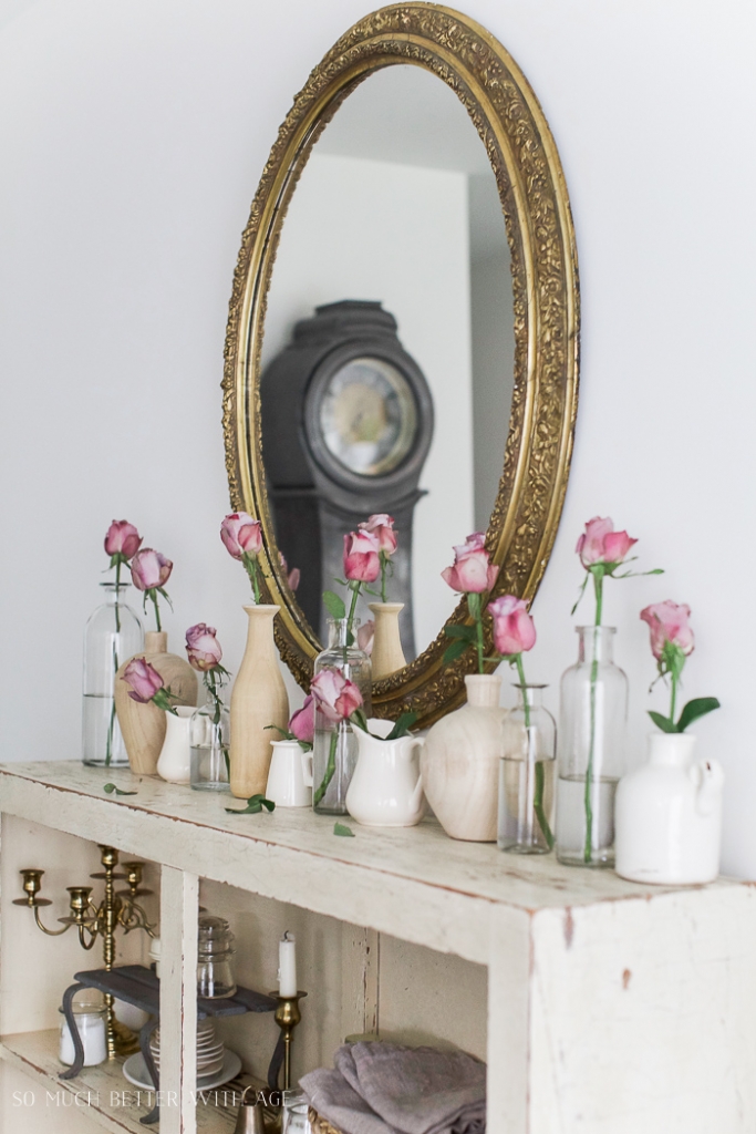 Roses in mini vases in front of mirror on cabinet. 