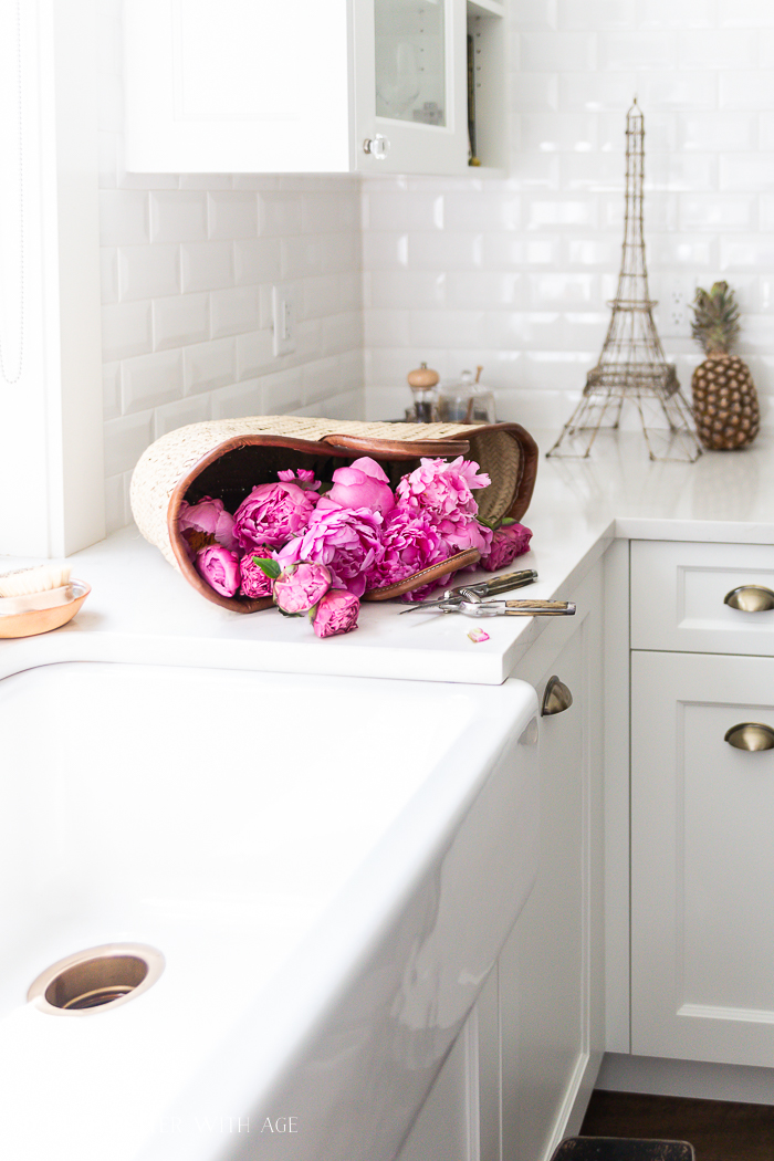 A basket is on the counter with pink peonies in it.