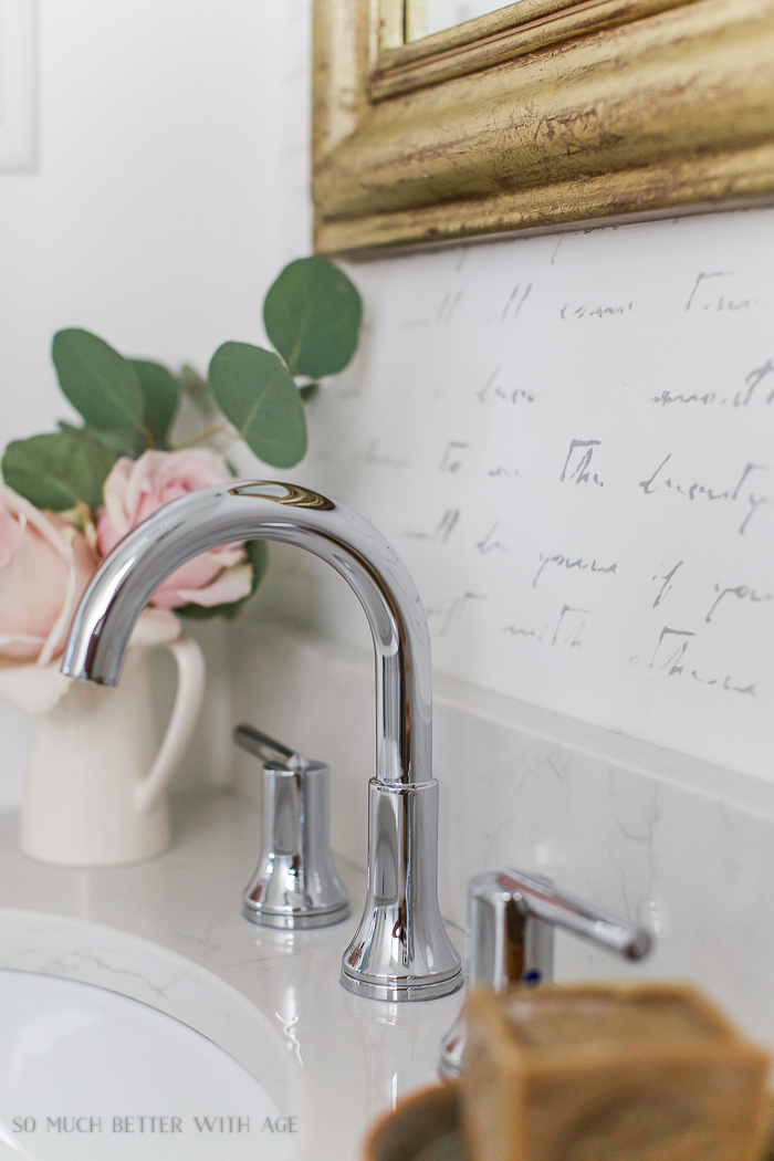A faucet and pink roses in the bathroom.