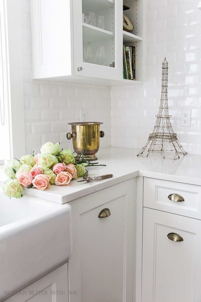 White kitchen with pink and green flowers on the counter and an Eiffel Tower on the counter.