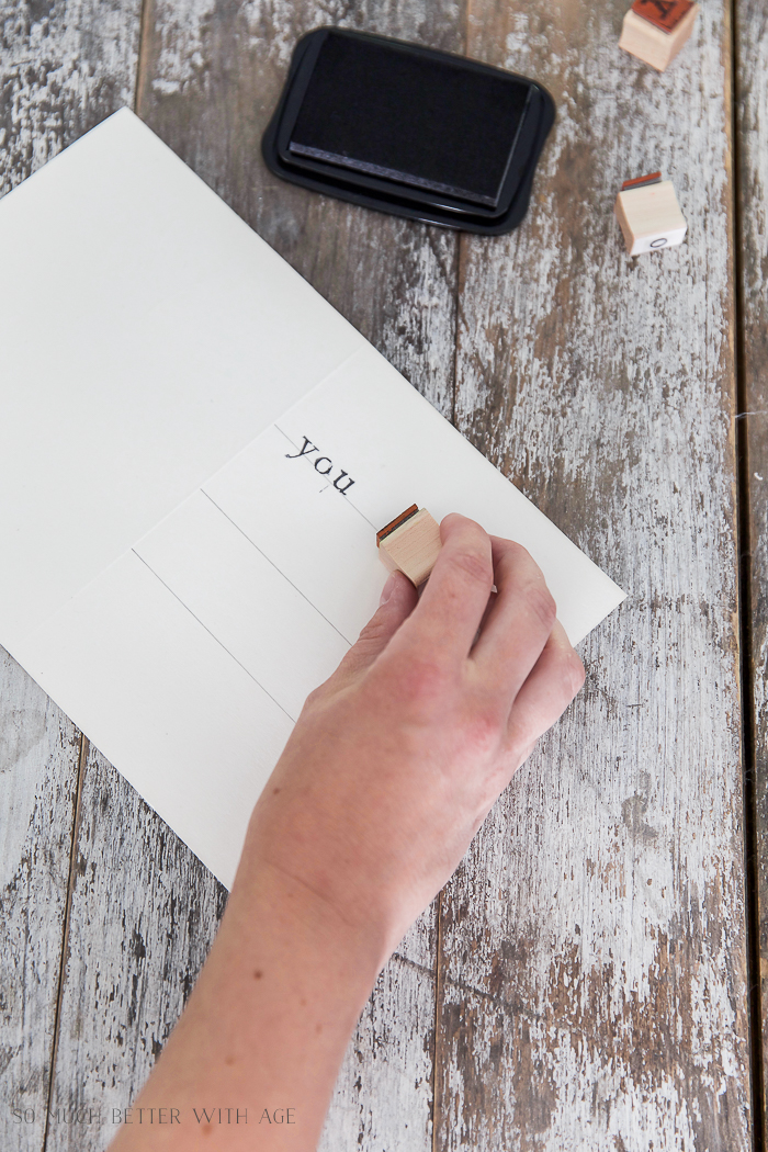 Stamping the word YOU onto the white piece of paper with pencil lines.