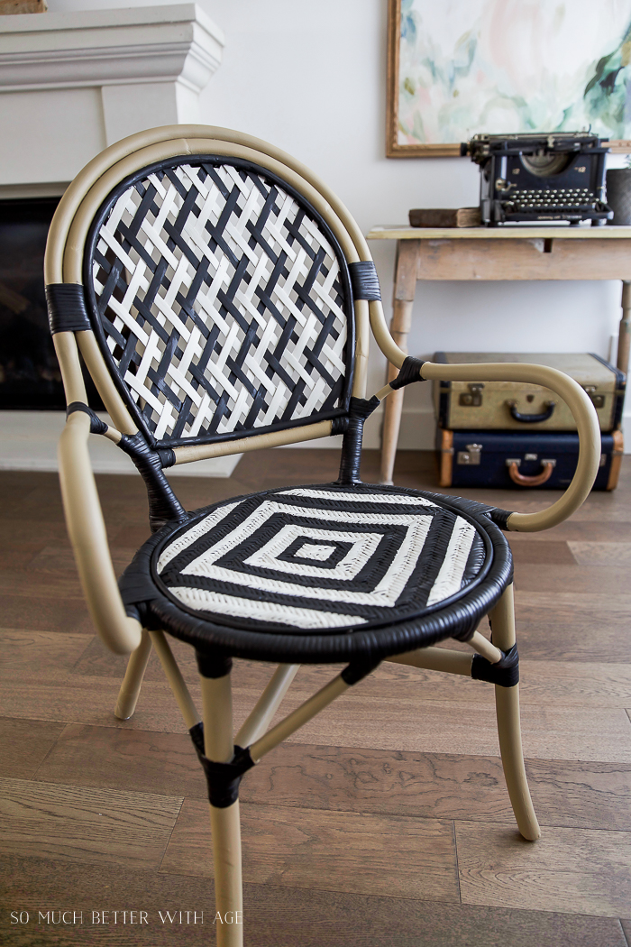 The chair in the living room with a small wooden desk behind it with an antique typewriter on top and suitcases underneath.