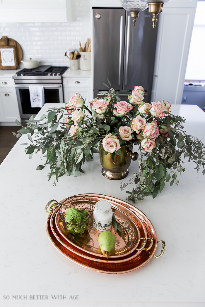 Copper platters on white kitchen island and flowers in a vase beside it.