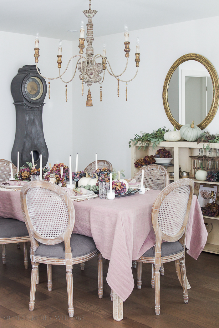 Blush pink tablecloth on table with pink and purple dried flowers and white candles.