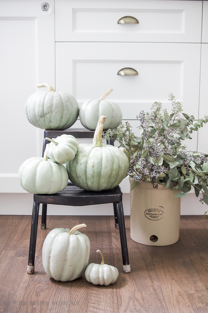 Heirloom pumpkins on a step ladder with a crock filled with eucalyptus beside it.