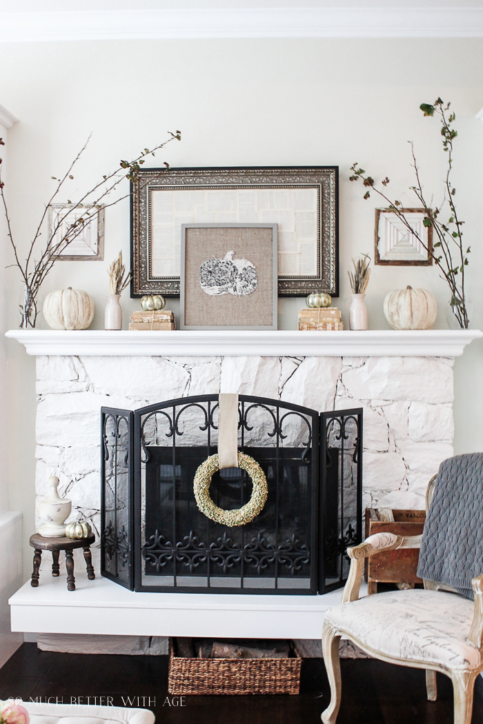 White fireplace mantel decorated with vintage books, pumpkins, branches, and vintage mirror.