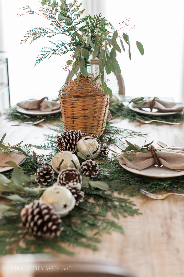 Cedar branches on the table with bells and pinecones.
