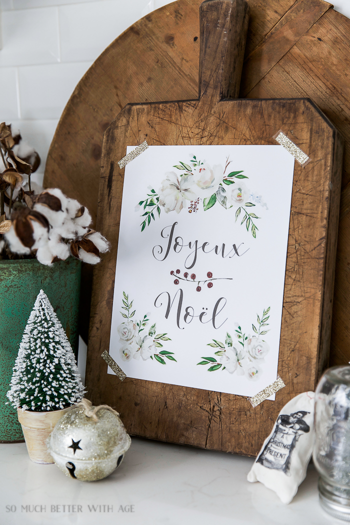 Joyeux Noel printable taped to a bread board with flowers and leaves on the printable.