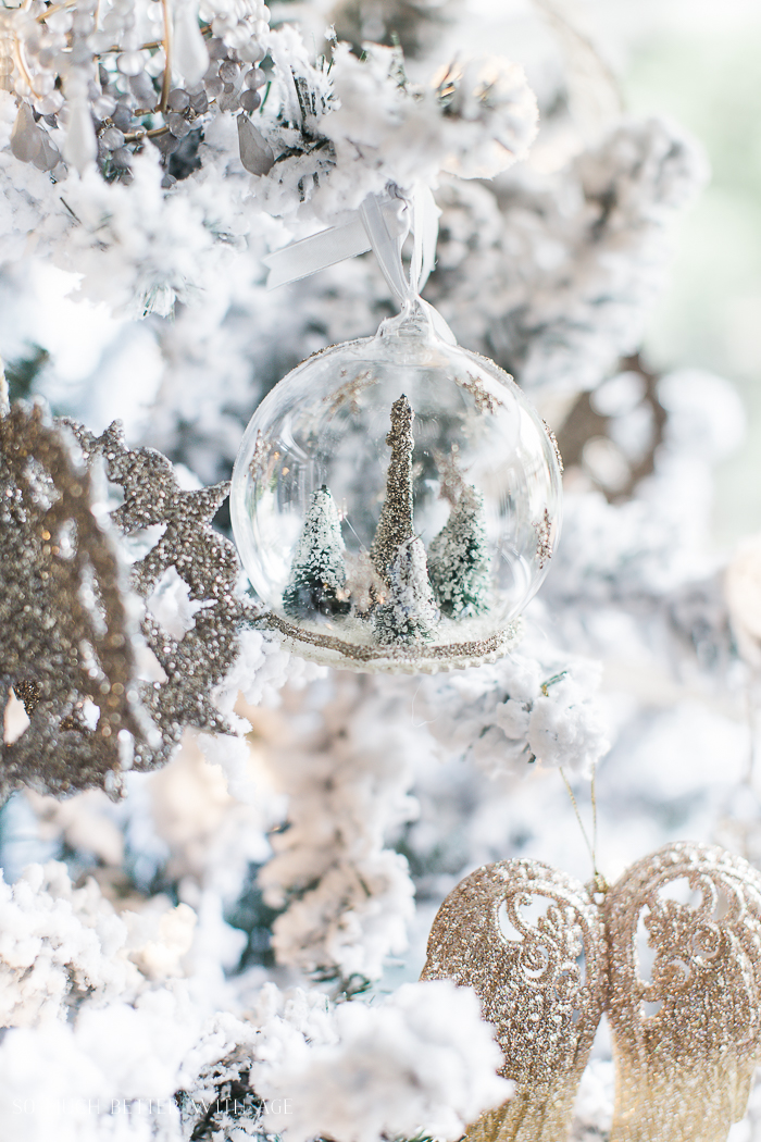 Snow globe ornament with mini trees inside it on a Christmas tree.