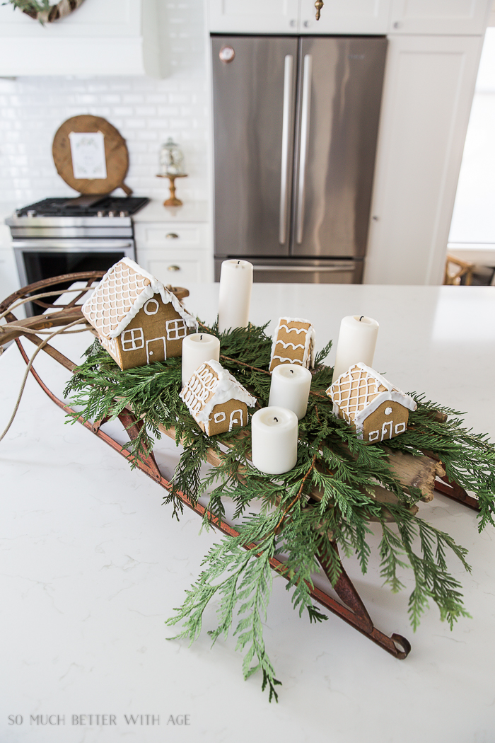 Gingerbread houses with candles, cedar branches on sled.