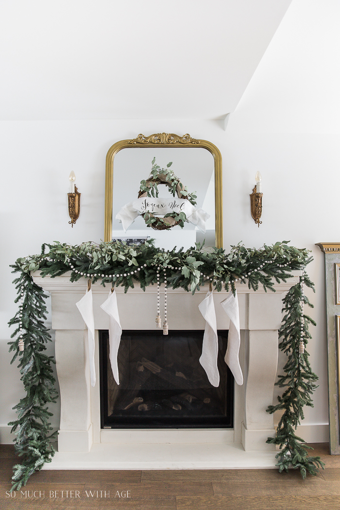 Fireplace with white stockings and greenery around it.