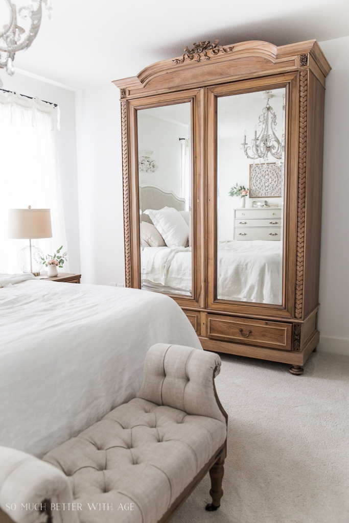 Ornate tall gorgeous wooden armoire with mirrors on front and French chandelier in bedroom. 