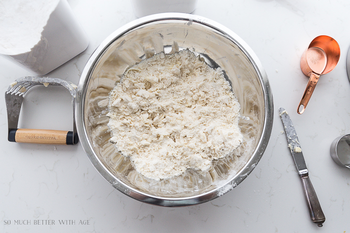 Metal mixing bowl with pastry blender beside it and a knife and brass measuring cup.