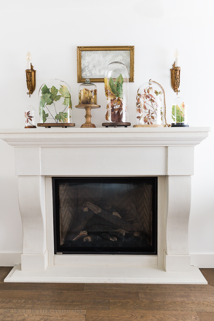 White fireplace mantel with cloches on top and wall sconces beside them.