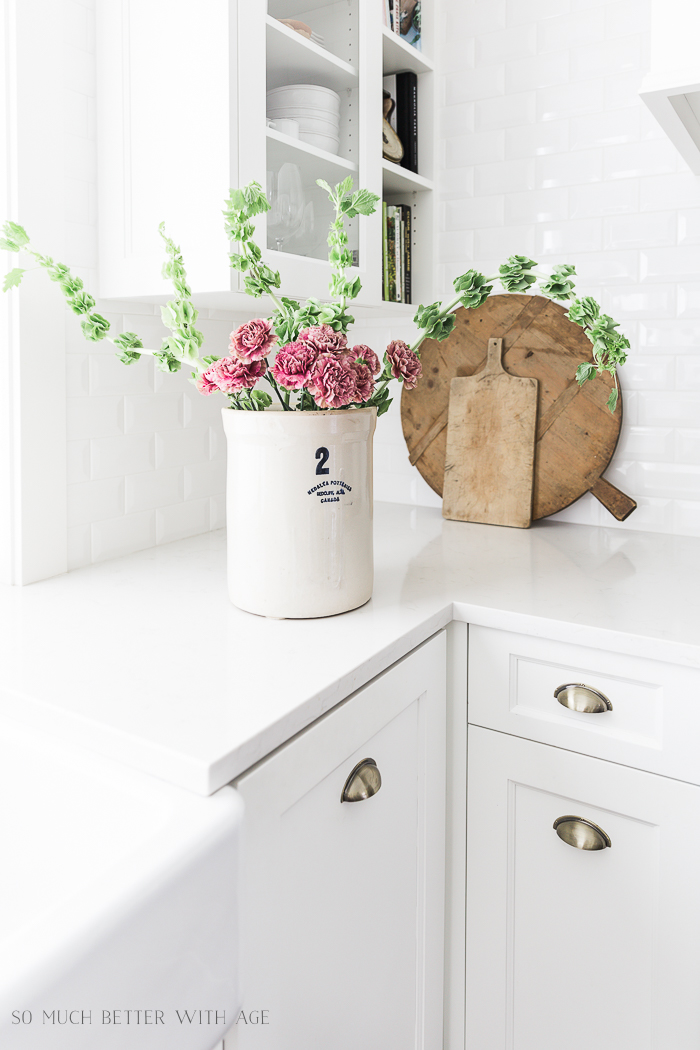 White Frech kitchen with crock on counter and pink and green flowers in crock.