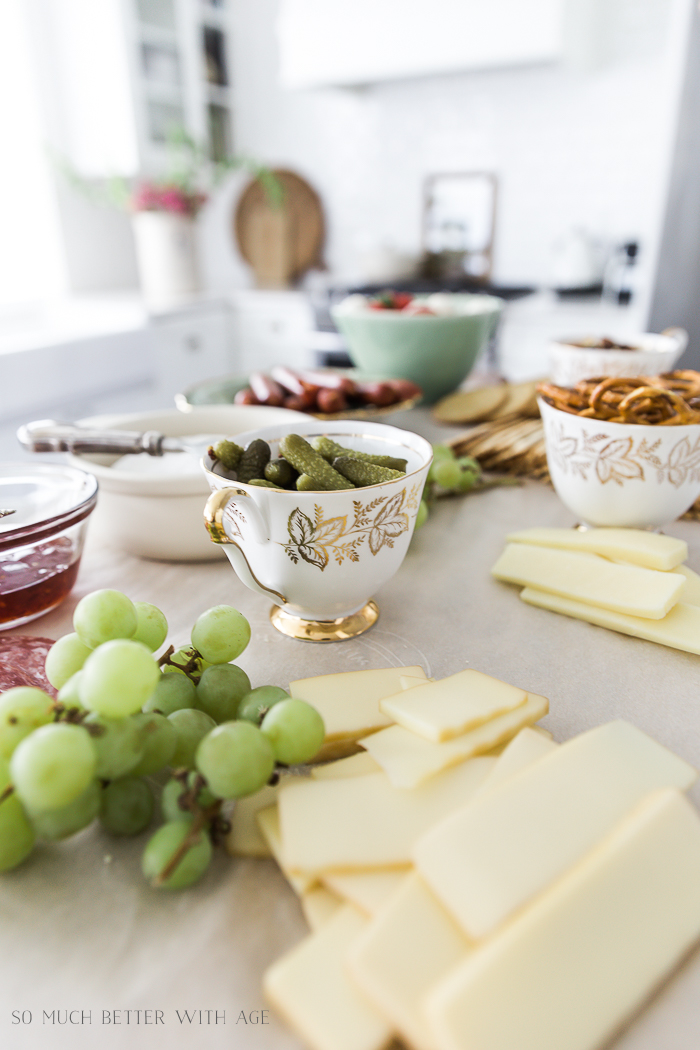 Tea cups filled with pickles and pretzels on the charcuterie board.