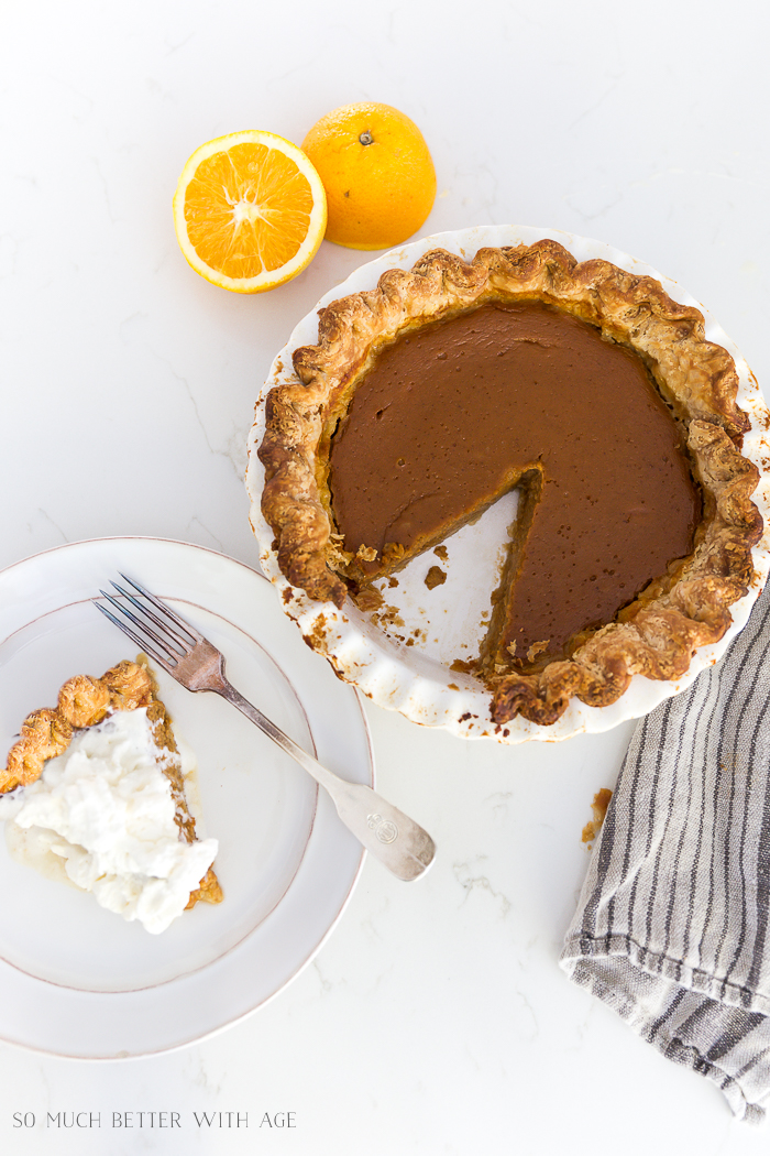 Pumpkin pie in pie plate and also a slice on a white plate with whipping cream on top.