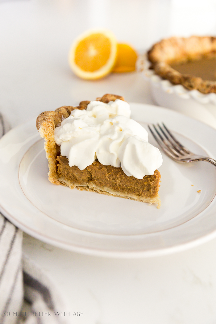 Pumpkin pie with whip cream on a plate with a fork and an orange cut in half in background.