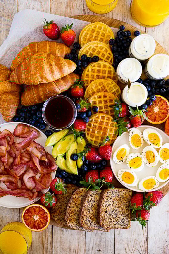 Breakfast board with croissants, boiled eggs, bacon, yogurt, fruit, and toast from Simply Delicious Food. 