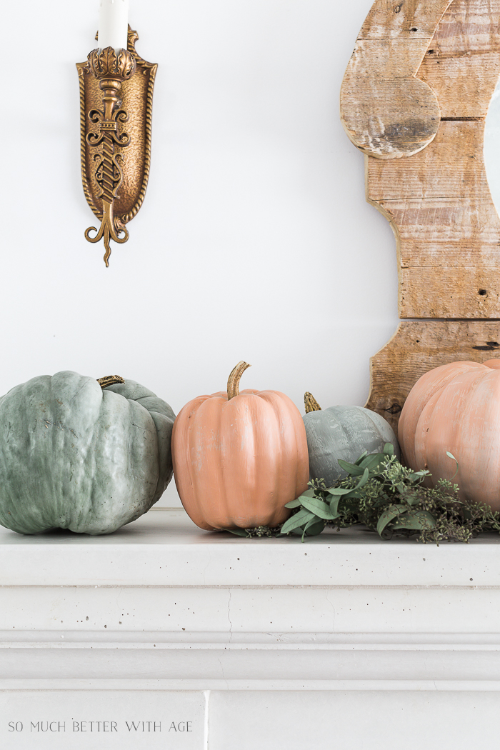 Four pumpkins in a sage green and soft orange on the mantel with eucalyptus.