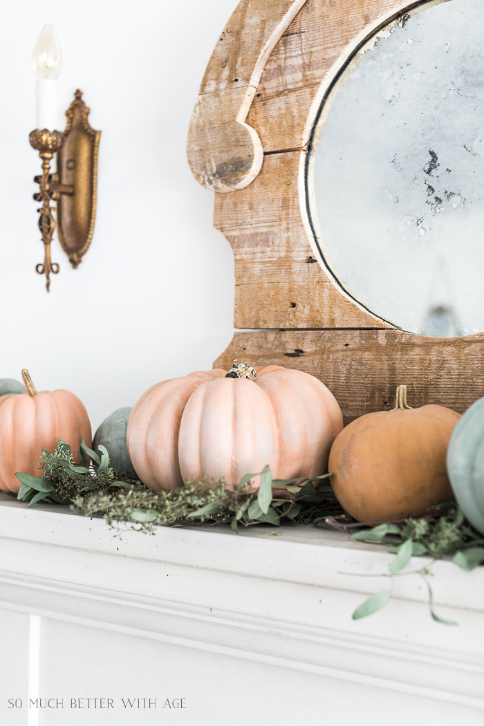 White fireplace mantel with muted colored pumpkins on it and a mirror behind them.