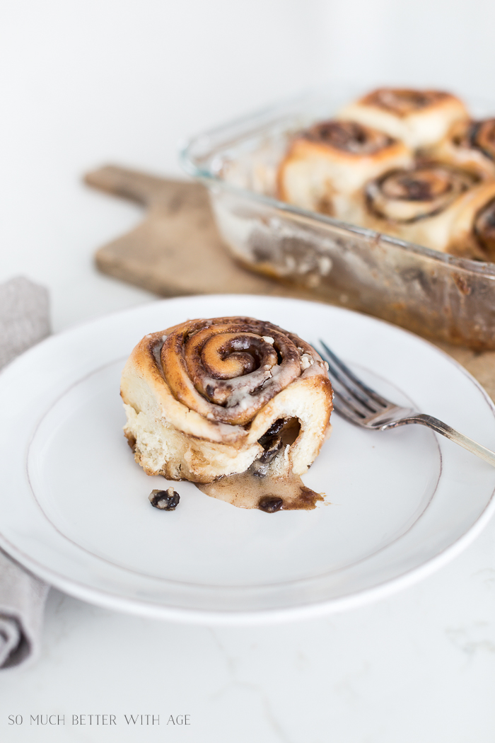 A gooey cinnamon bun on a white plate with a fork next to it.