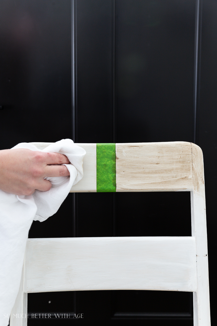 Using a white cloth to wipe off the wax on one side of the chair.