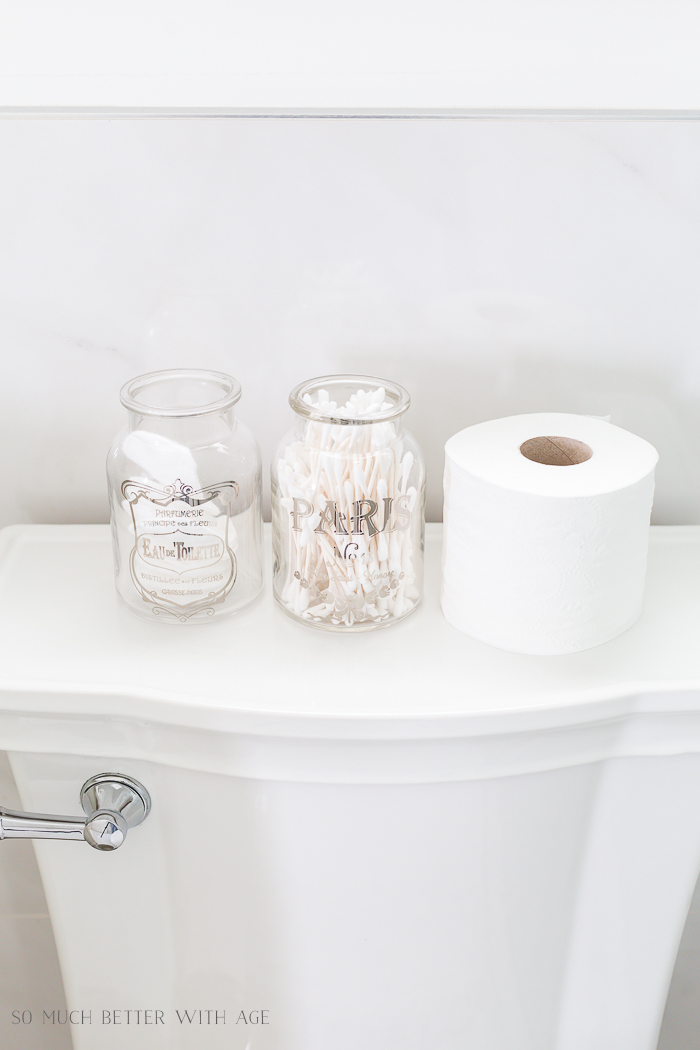 Glass jars filled with toiletries on the top of the toilet.