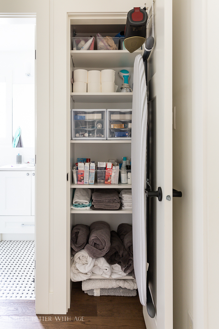 Organized bathroom closet with ironing door and iron hanging on inside of door. 