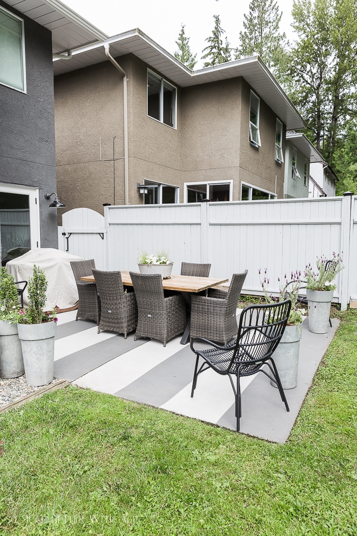 Backyard with stripes painted on concrete and grey painted fence. 