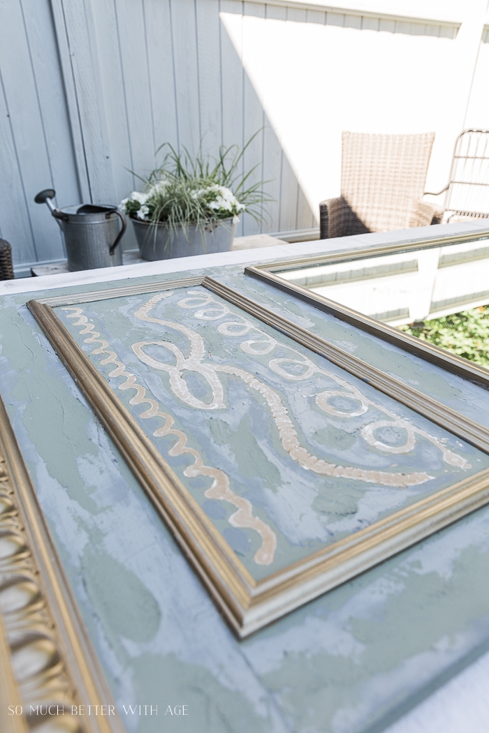 Green, gold and grey mirror laying flat on table outside. 