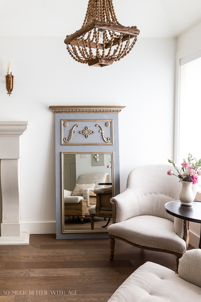 Trumeau mirror leaning against a wall in living room in front of linen chair. 