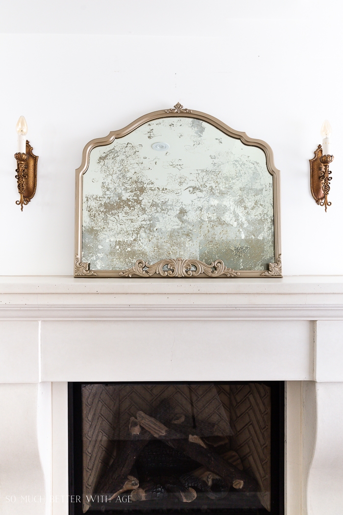 Antique mirror on fireplace with antique wall sconces. 