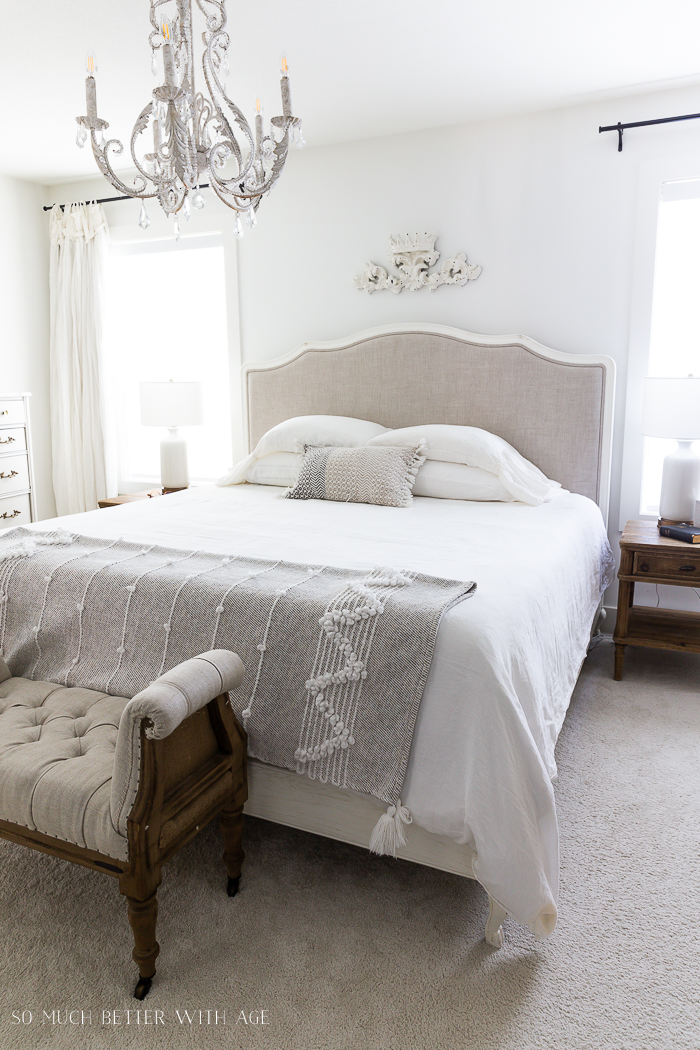 White linen bed with chandelier in bedroom. 