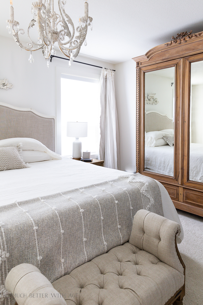 Large wooden armoire in bedroom with white linen duvet and chandelier. 