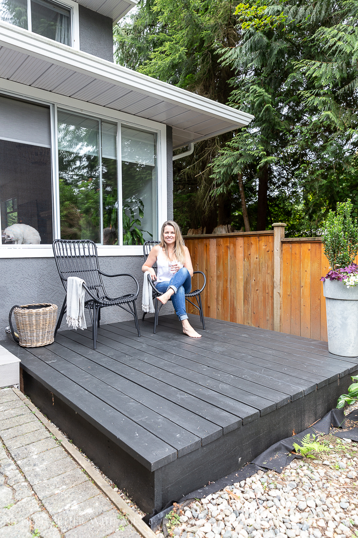 Woman sitting on black deck in front of house. 