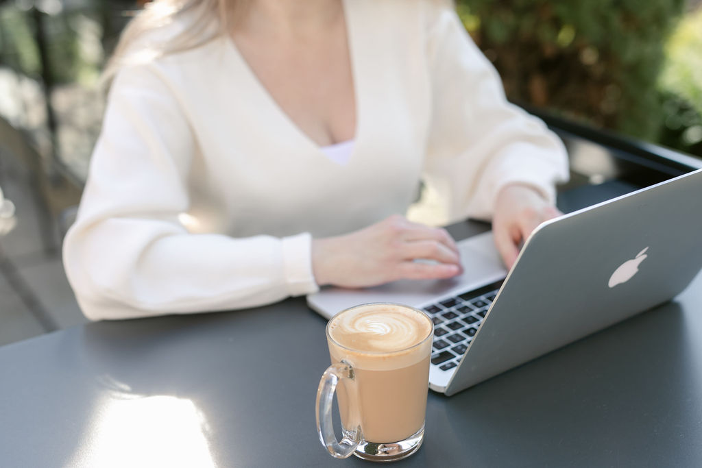 Woman typing on laptop with latte.