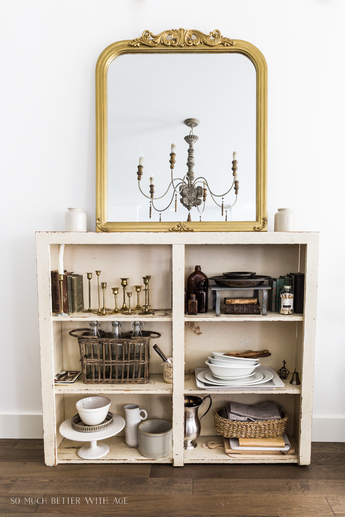 Collection of vintage items on old bookshelf with large French gold mirror leaning on top. 