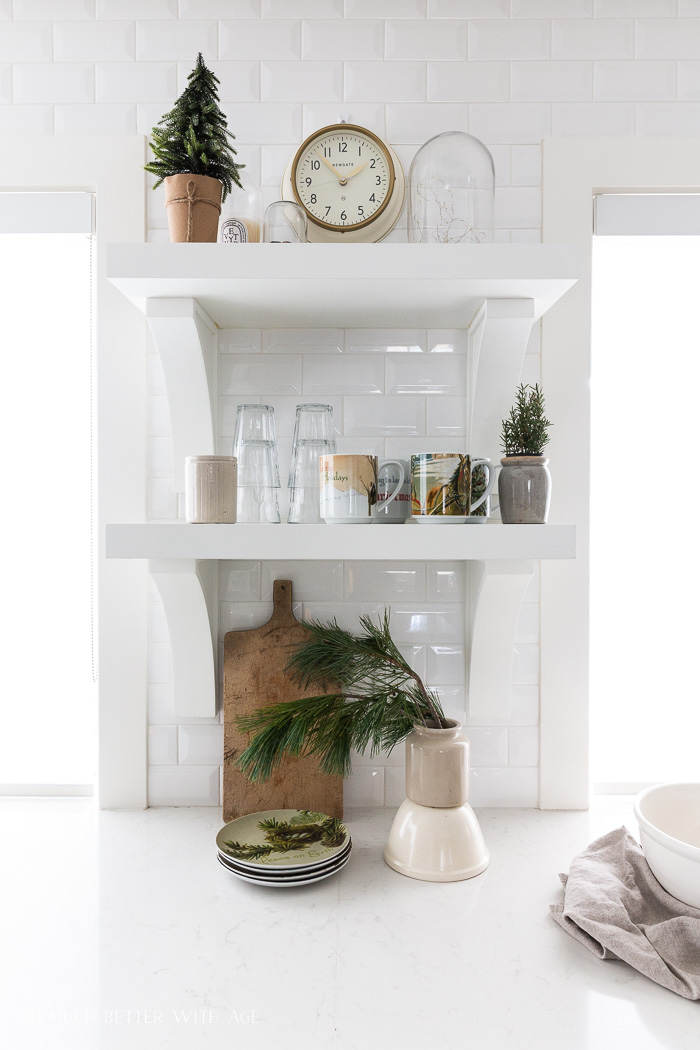 White kitchen shelves with Christmas mugs and pine tree clippings. 