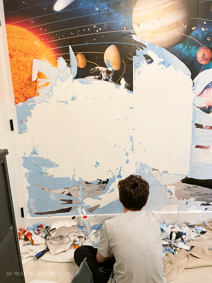 Boy removing wallpaper of space scene from off of wall. 