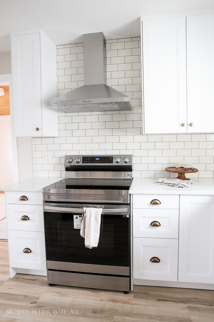 White kitchen with wall of cream subway tile and floating hood vent. 