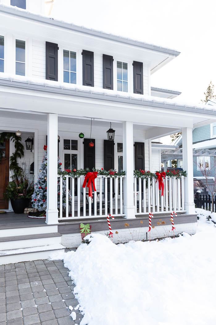 Big porch on white house with black shutters with red bows for Christmas. 