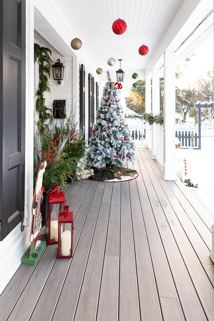 Christmas tree on front porch of farmhouse and ornaments hanging from the ceiling. 