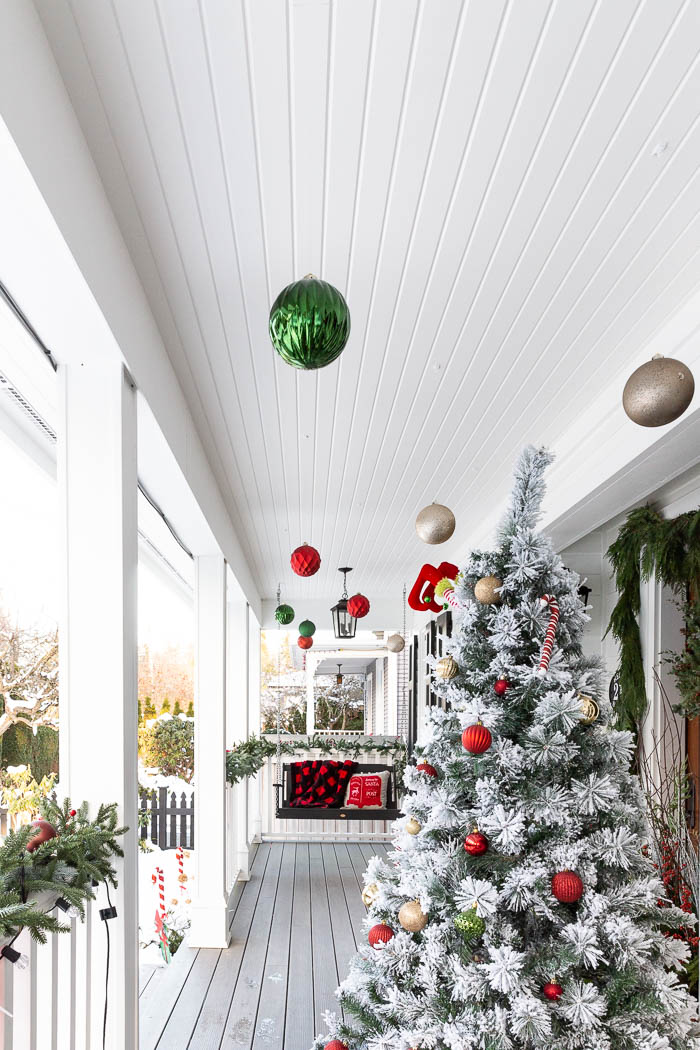 Ornaments hanging from the porch ceiling with a Christmas tree on porch. 