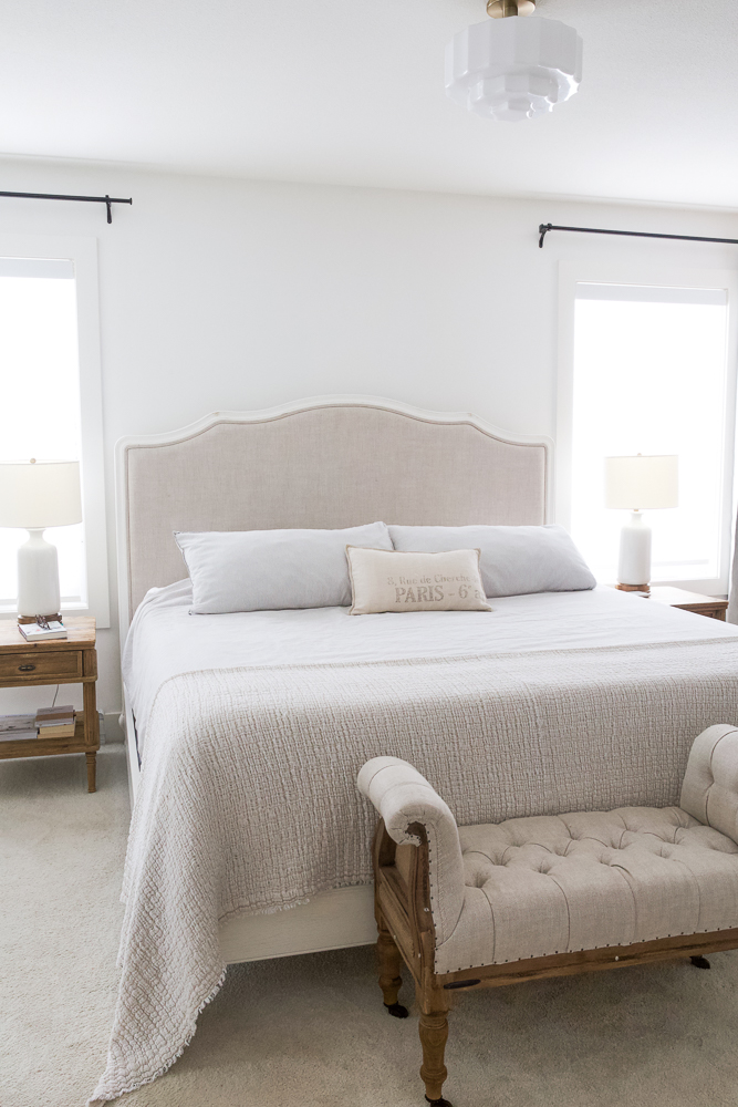 Curved French upholstered bed in white painted bedroom with tufted bench in front of it. 