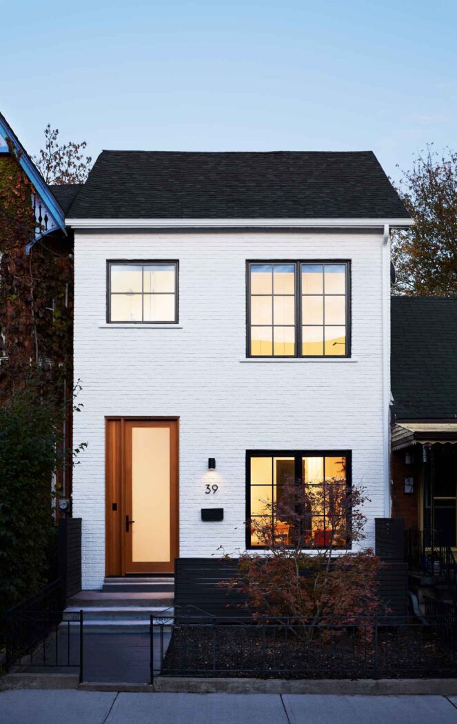 Brick house painted white with black windows and wood door. 