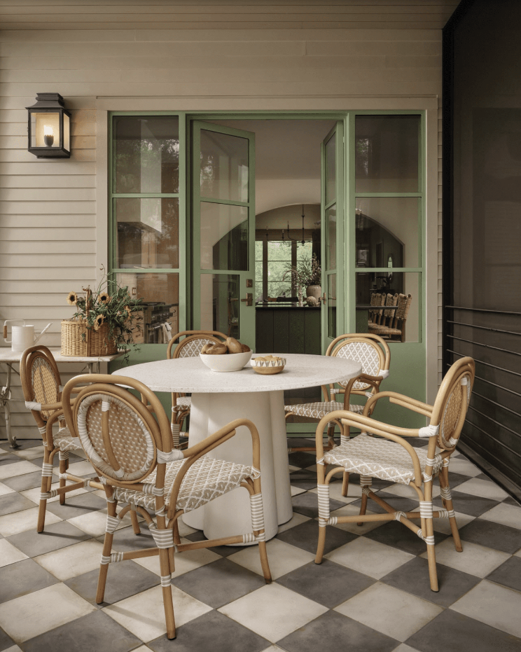 Checkerboard tiled patio with French bistro chairs around round table with green painted French doors. 