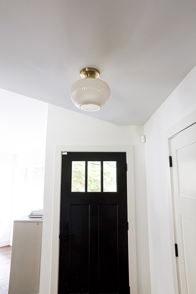 Entryway with black door and antique brass flush mount with ribbed champagne milk glass.